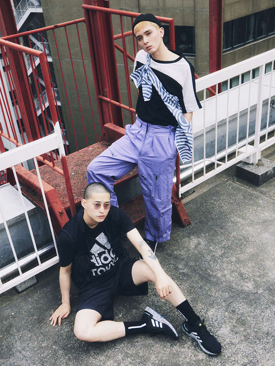 Two young men wearing items from HIROKO TAKAHASHI COLLECTION are standing on top of an office building in Tokyo.