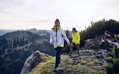Three people wearing TERREX functional jackets are enjoying a chill hike on a rocky mountain.
