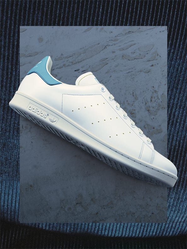 A white Stan Smith sneaker with blue detail against neutral background.
