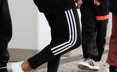 A close-up of a group of people's legs, all wearing adidas pants.
