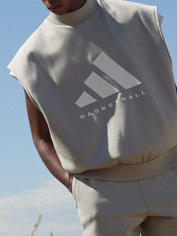A rear view of someone adjusting the hood of their light green sweatshirt with a white adidas Basketball logo in front of a bright blue sky.