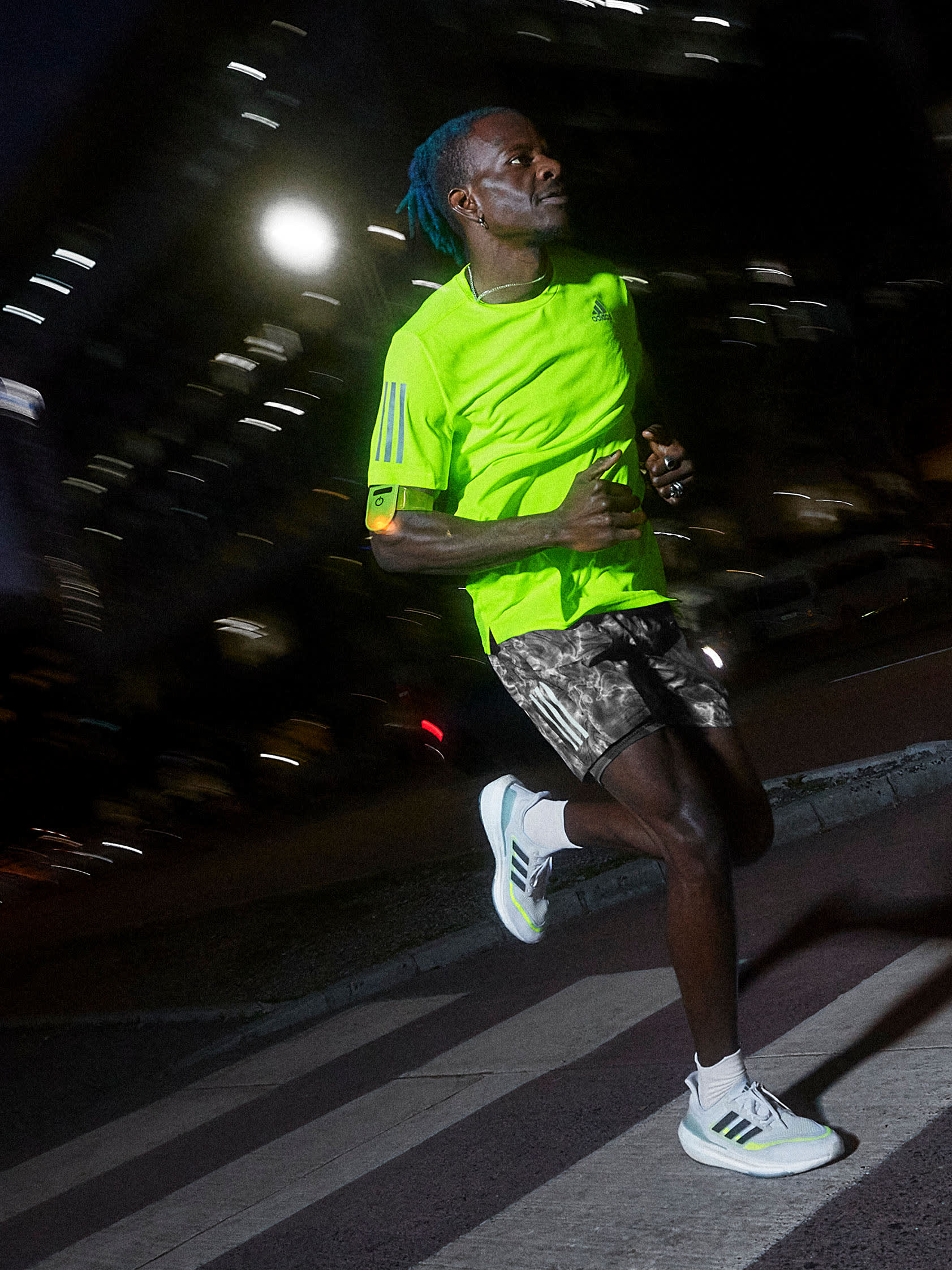 A man wearing a lime green shirt running at night wearing Ultraboost shoes