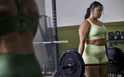 Female lifting weights and wearing a green adidas set of sports bra and shorts