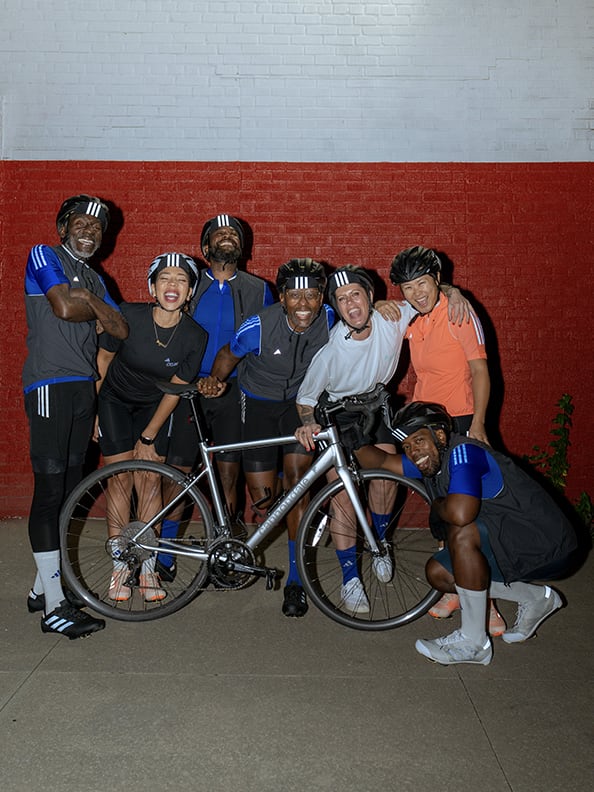 A GROUP OF PEOPLE SMILING BEHIND A SILVER BICYCLE