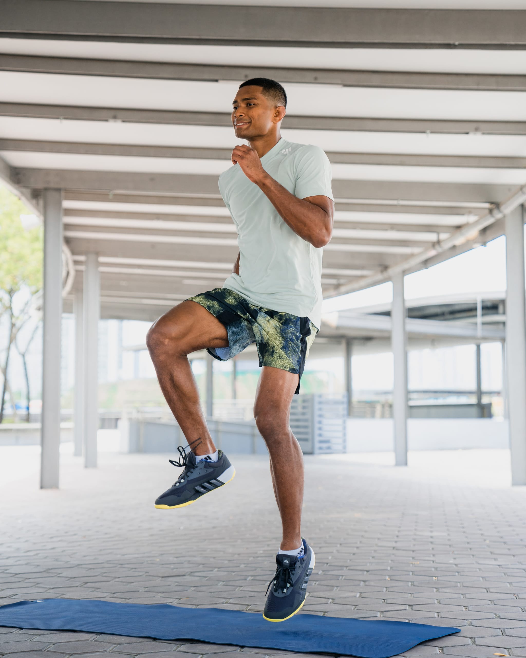 A non-binary athlete in workout gear doing a lunge in front of a bright pink and turquoise background.