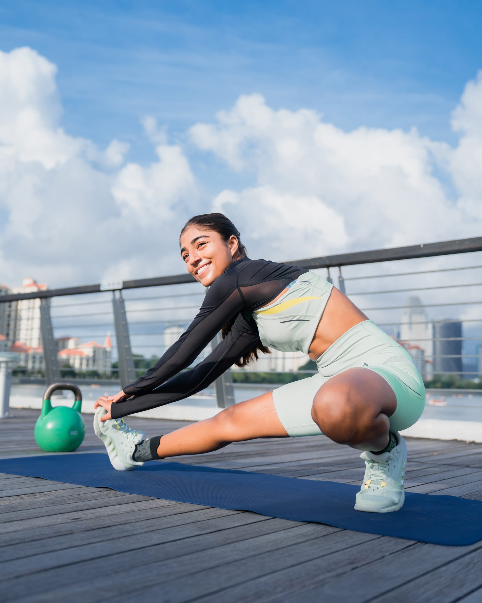 Woman in workout gear working out, in front of a bright blue background covered with smiley graphics.