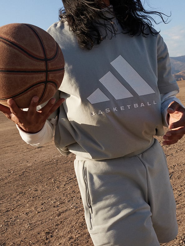 A person holding a basketball in their right hand wearing a grey adidas Basketball t-shirt