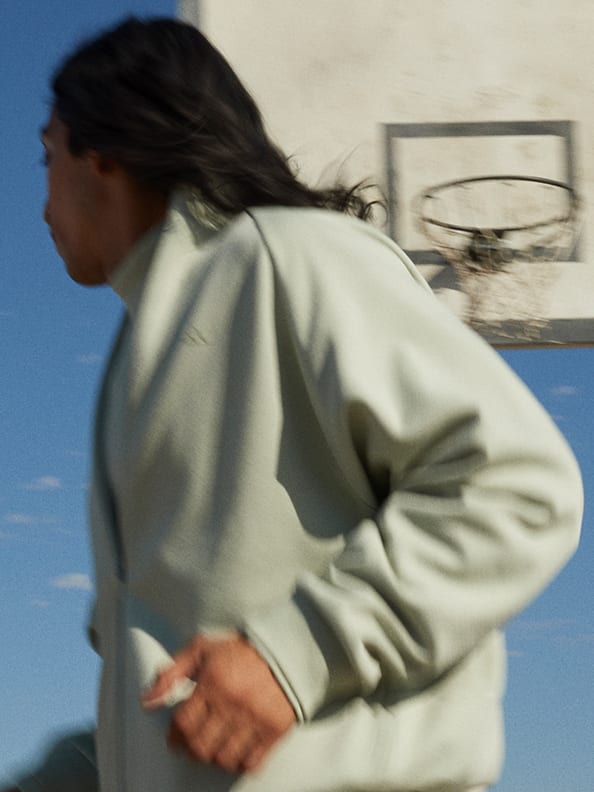A blurred image of someone in grey shorts and a short sleeve shirt with white adidas Basketball logo dribbling a basketball