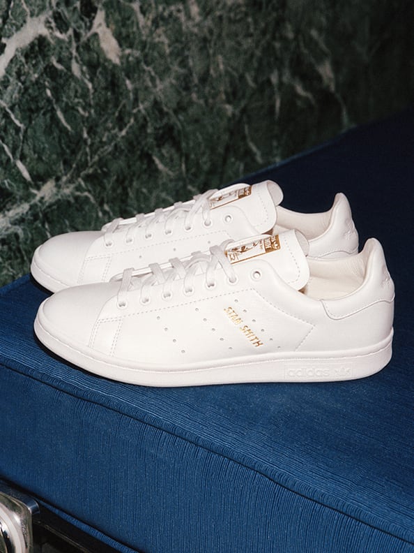 A pair of white Stan Smith shoes against a dark background.