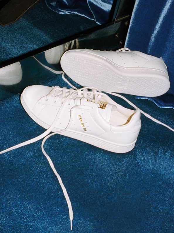 A pair of white Stan Smith shoes against a dark background.