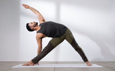 A man is holding a yoga pose wearing a yoga tank top and bottoms from the Make Space yoga collection.