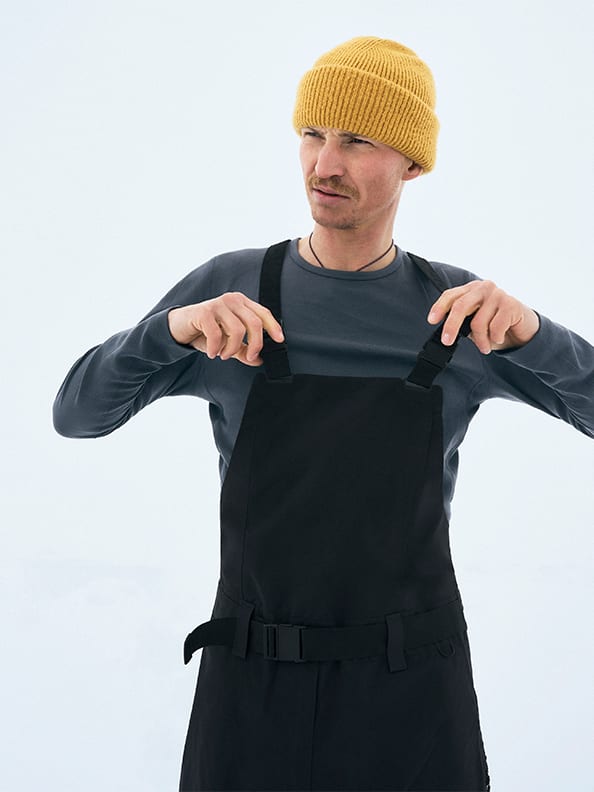A person wearing a yellow beanie and black overalls