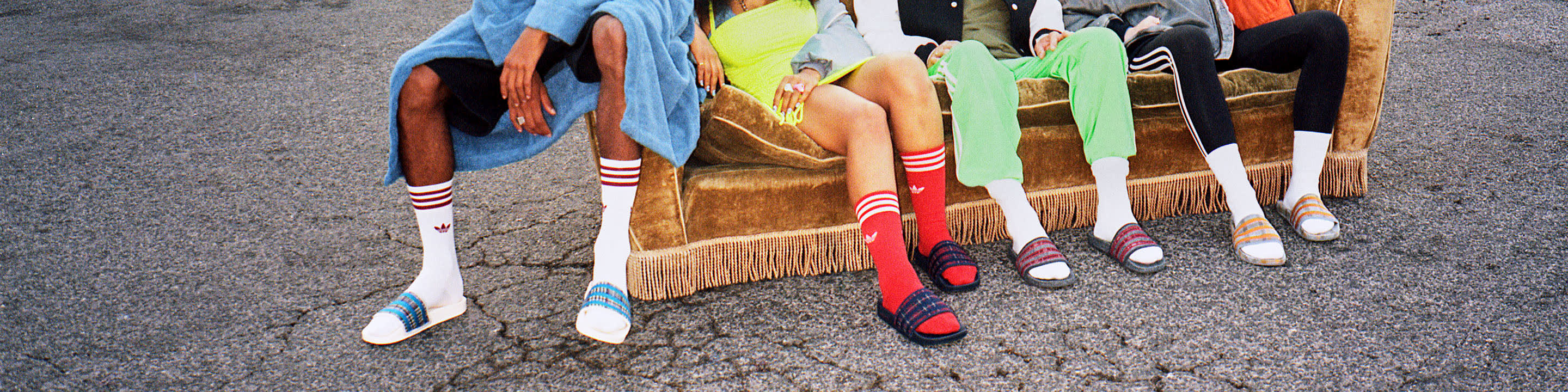 Four people from waist down sitting in a row on an old couch outside on the street.