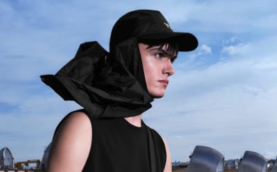 A man wears a black Y-3 cap and scarf under a blue sky.