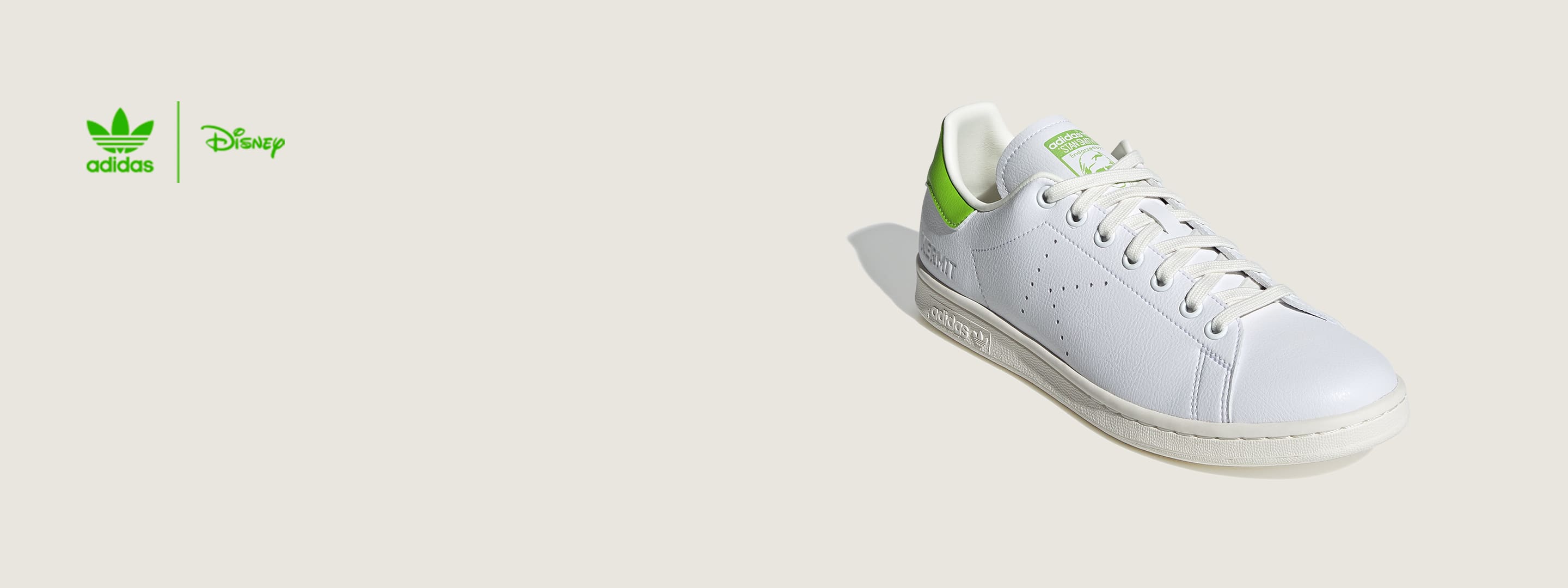 Stan Smith shoes stand upright. A plastic bottle cap leans against one. The years 1973 and 2021 are typed beside the shoes.