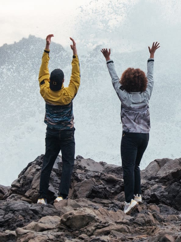 A woman and a man playing with water wearing the adidas TERREX x © National Geographic collab jacket, pants and shoes.