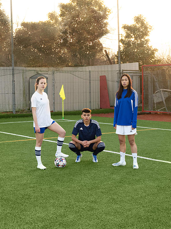 Image of 3 players, 2 females, one male posing on the pitch, kits on, female on the left hand side has the ball.