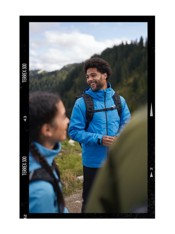 Serge Gnabry hiking with friends and smiling wearing TERREX gear with a mountain background.