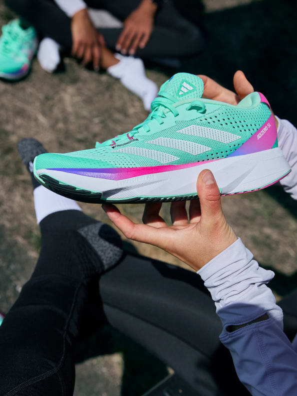 An image of a runner sitting down, holding the green women’s Adizero SL shoe