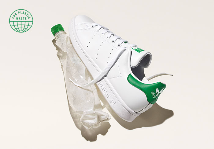 A Stan Smith shoe next to a crumpled water bottle on a white background.