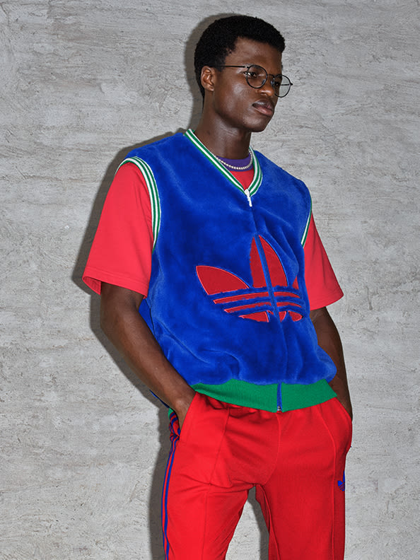 A male model wearing a velvet sweater vest and red trackpants from the latest adicolor collection with Gazelle shoes
