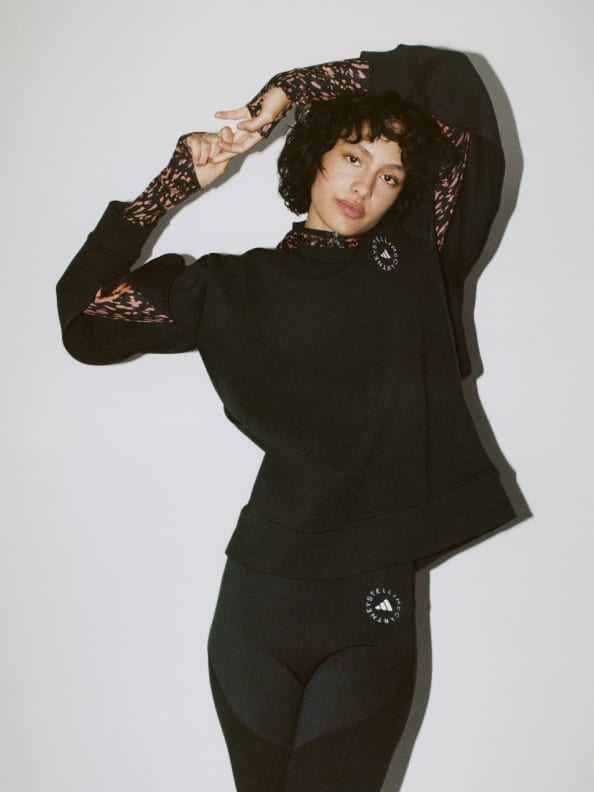 A model posing standing up. She wears a layered look of the Long sleeved hoodie underneath the black sweatshirt She finishes off the look with the tights in Black and Dove grey.