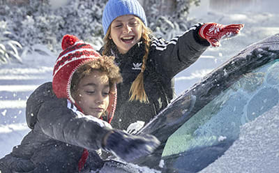Kids drawing on a snow covered car.