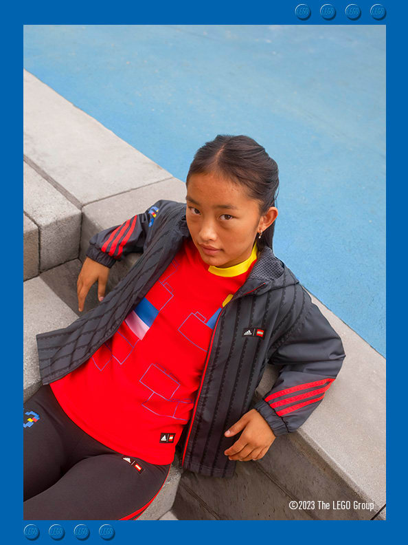 A young girl lying on concrete steps, looking confidently wearing adidas LEGO® sweatshirt, trousers and footwear.