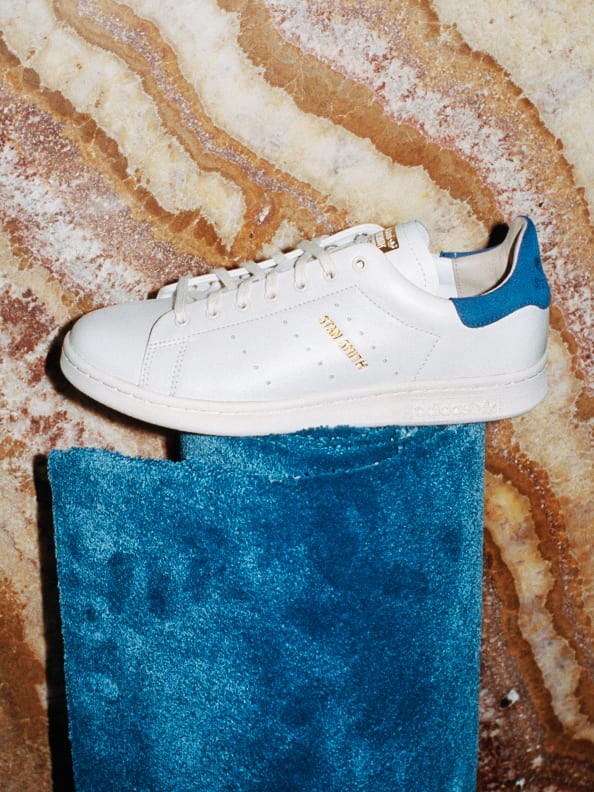 A white Stan Smith shoe positioned on top of a rolled up carpet.