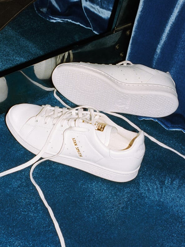 A pair of white Stan Smith shoes against a dark background.