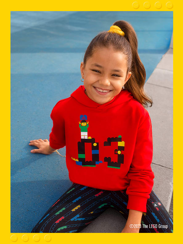 A little girl sitting on concrete steps, smiling confidently wearing adidas LEGO® hoodie and bottoms.