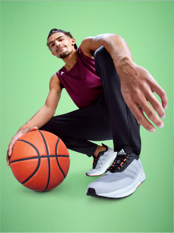Basketball player Trae Young squats in a low pose, holding a basketball.
