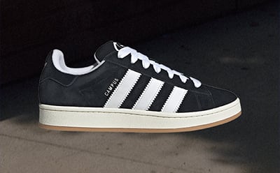 A pair of black and white sneakers with a gum sole sits on a dark surface, with a plain background.