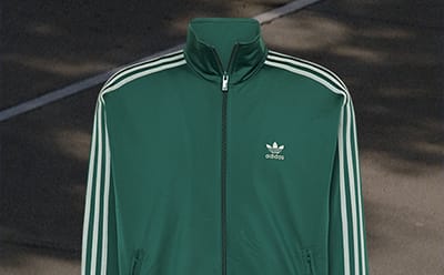 A green Adidas jacket with white stripes on a dark background.