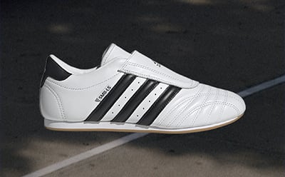 A white and black sneaker with a distinctive design sits on a dark surface, with a blurred background.