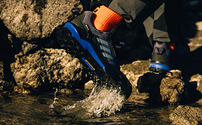 A person wearing dark clothing and bright-colored gear is walking through a shallow stream, with water splashing around their feet.