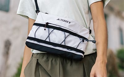 A person wearing a white Adidas backpack stands in front of a blurred background, with the backpack's distinctive branding and design visible.