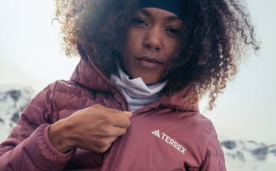 A person with curly dark hair wearing a burgundy jacket stands in a snowy outdoor setting.