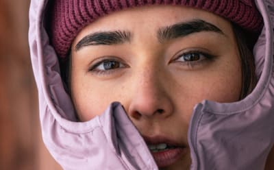 A person wearing a pink hat and scarf, with a serious expression on their face, appears to be the focus of the image.