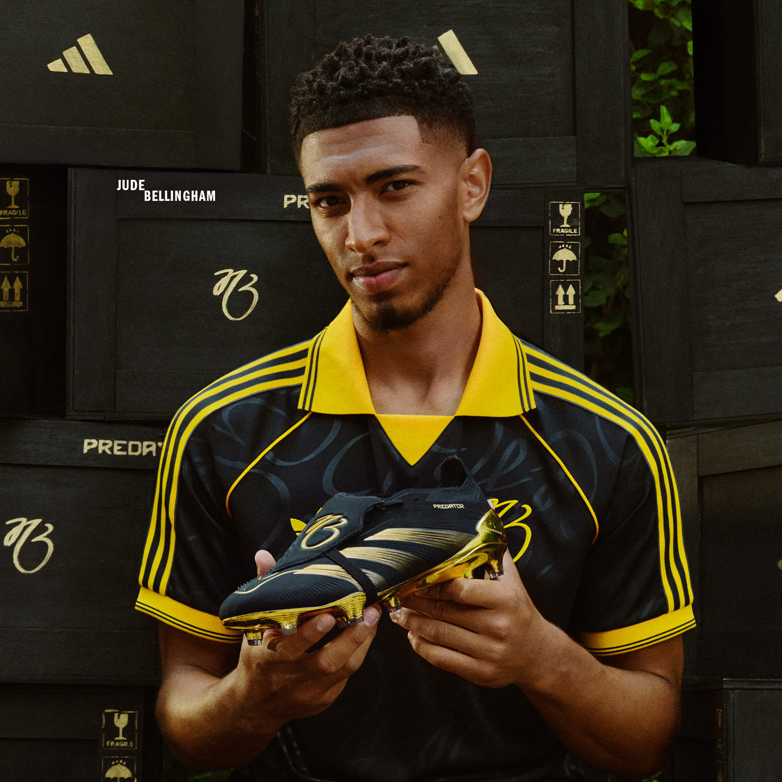 A young man wearing a yellow and black sports jersey is holding a soccer ball in front of a dark background with Adidas branding.