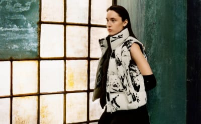 A model is pictured in front of a raw industrial interior backdrop wearing a Y-3 gilet.
