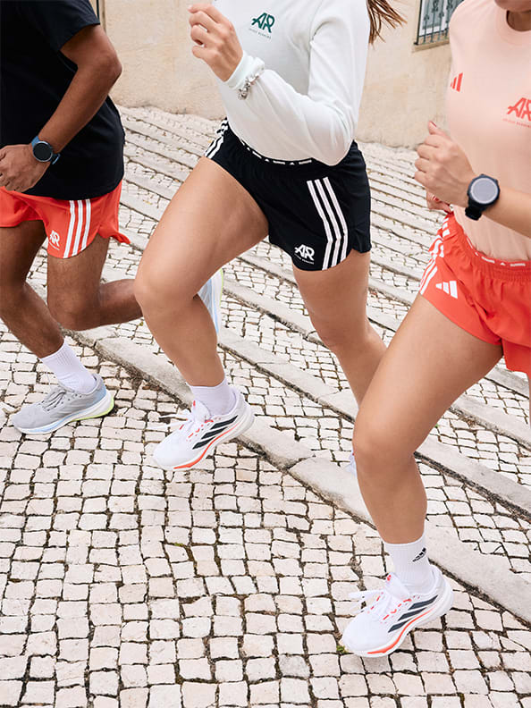 Three people, two women and one man, running up stairs in an urban setting. The image is cropped to only feature their shoes up to their shoulders