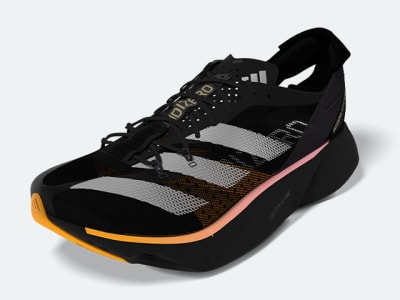 The image shows a close-up view of a black and pink athletic shoe, with a textured upper and a white sole visible in the background.