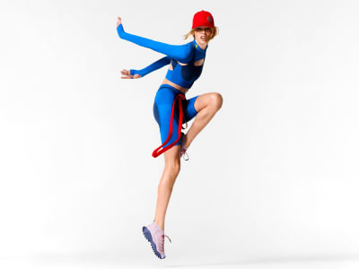 A person in a blue and red costume is striking a dynamic pose, with one leg raised and arms extended, against a plain white background.