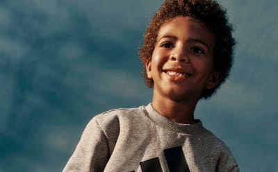 A smiling young person with curly hair against a blue sky background.