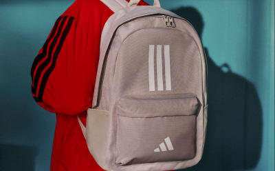 A gray Adidas backpack with the brand's iconic three-stripe logo is visible in the foreground, set against a vibrant red jacket hanging in the background.