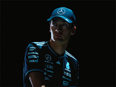 A person wearing a blue Mercedes-Benz cap and jersey stands in a dark setting, their face partially obscured.