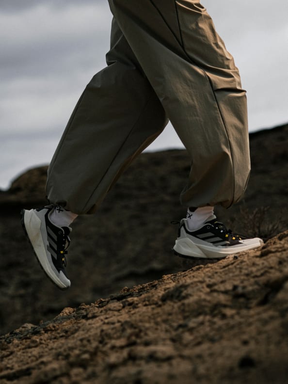 A person wearing khaki pants and black and white sneakers stands on a rocky, uneven terrain against a cloudy sky.