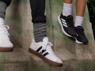 The image shows a close-up view of several pairs of feet wearing various athletic shoes, including black and white sneakers, standing on a concrete surface.