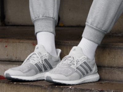 A pair of white and gray athletic shoes with laces and a mesh upper, resting on a concrete surface.